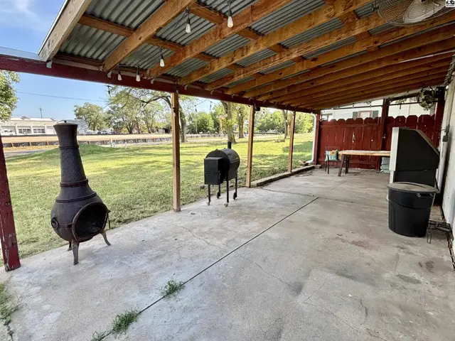 Covered patio with concrete floor, outdoor fireplace, grill, and picnic table.