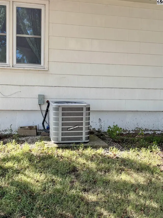 Exterior air conditioning unit sits on a concrete pad next to a white-sided house.
