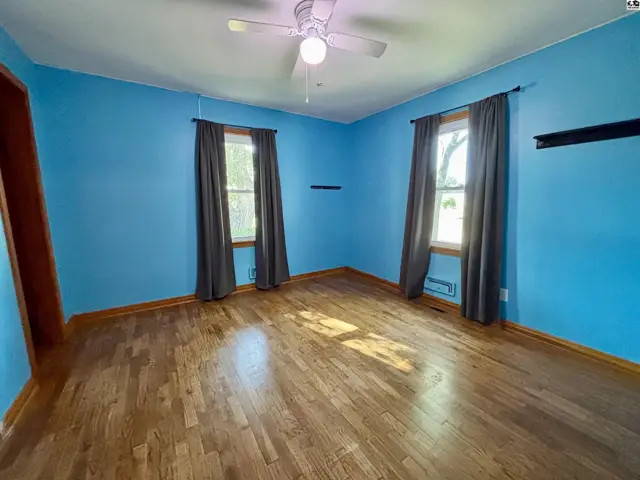 This room features hardwood floors, blue walls, and two windows with grey curtains.