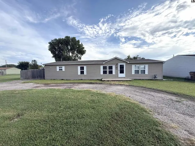 This single-story home features a tan exterior with white trim and a gravel driveway.