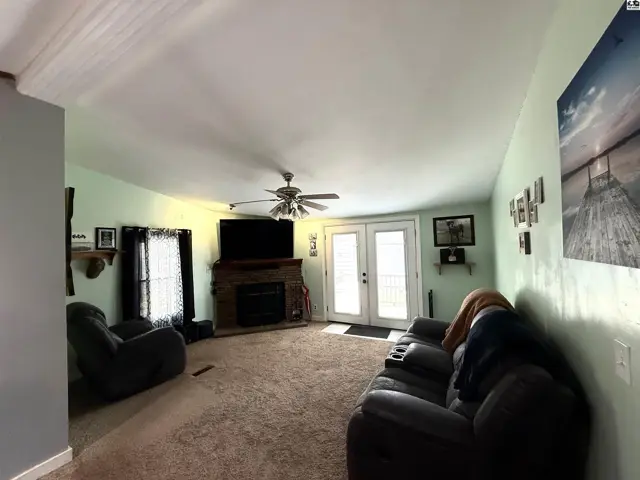 Spacious living room features a brick fireplace, ceiling fan, and double doors.