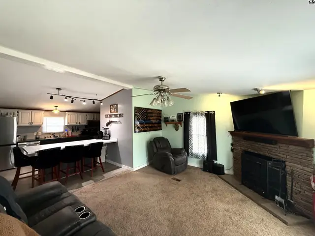 Spacious living area with a stone fireplace and adjacent kitchen with island seating.