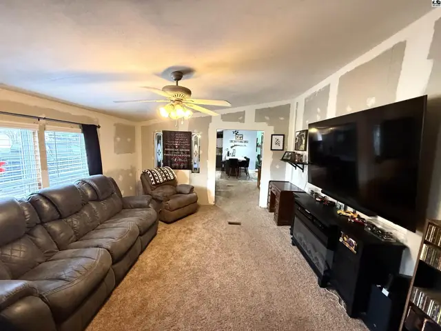 Spacious living room with plush carpet, a leather sofa, and a large television.