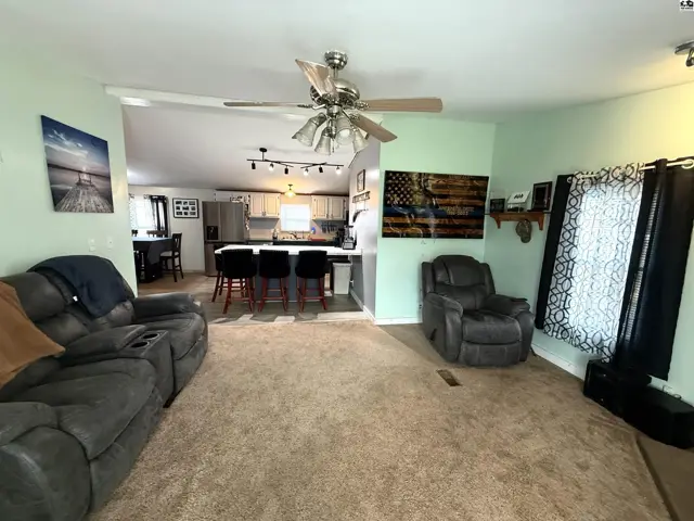 Carpeted living area opens to a kitchen with island seating and pendant lights.