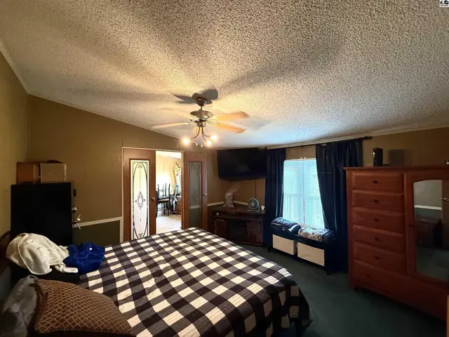 Spacious bedroom with a ceiling fan, large dresser, and access to a dining area.