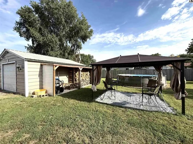 A detached garage and covered patio with an above-ground pool are situated on a grassy lawn.