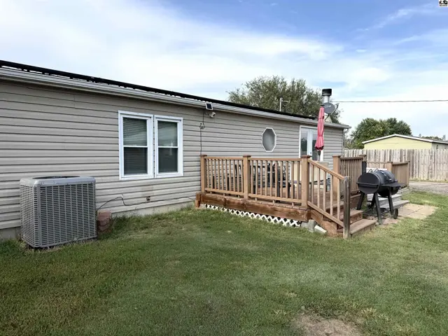 A wooden deck with a grill extends from the vinyl-sided home, surrounded by a grassy yard.