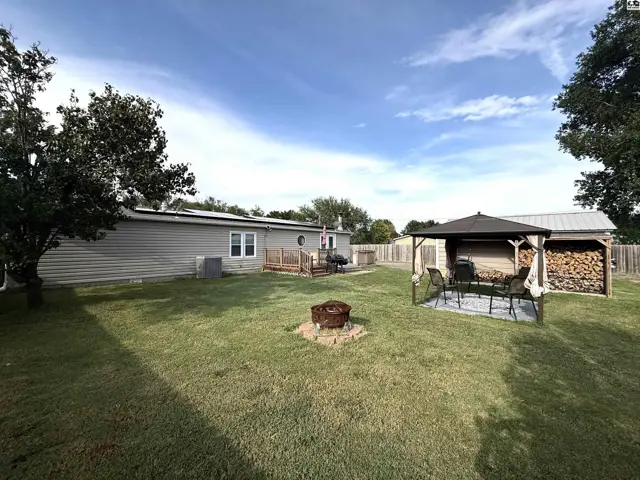 A fenced backyard features a deck, gazebo, fire pit, and storage shed.