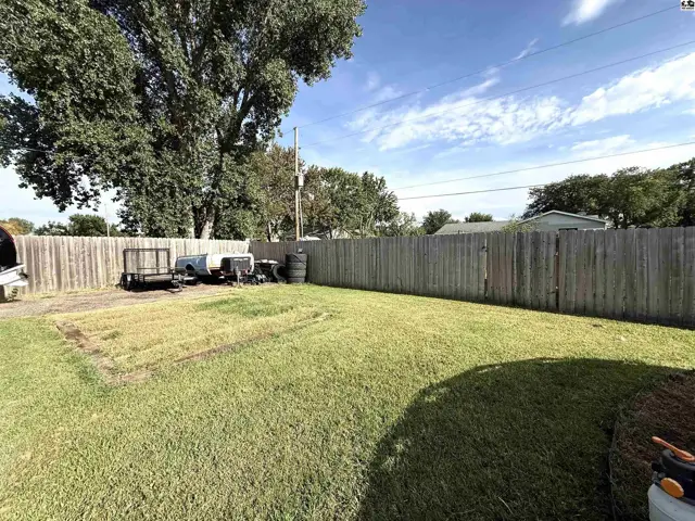 A wooden fence encloses a grassy yard with a cleared area and some stored items.