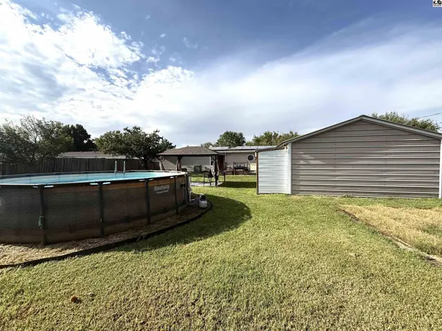 A large above-ground pool sits in a grassy yard with a detached metal garage.