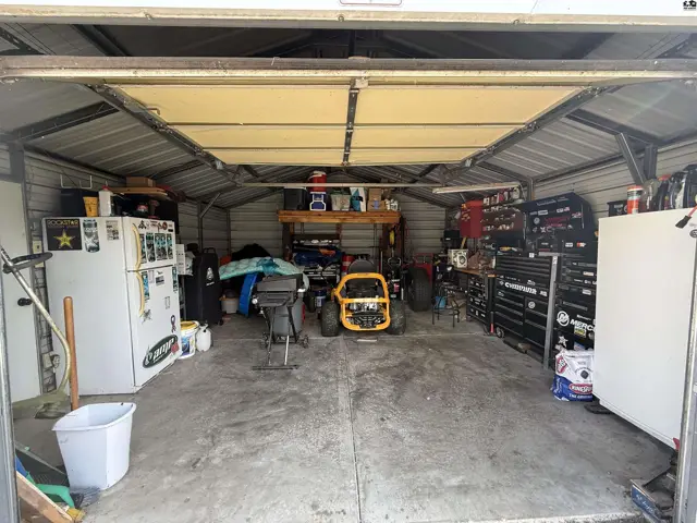 Metal garage with concrete floor, storage shelves, and a large overhead door.
