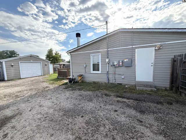 A detached garage with a white door sits on a gravel driveway next to a tan-sided home.
