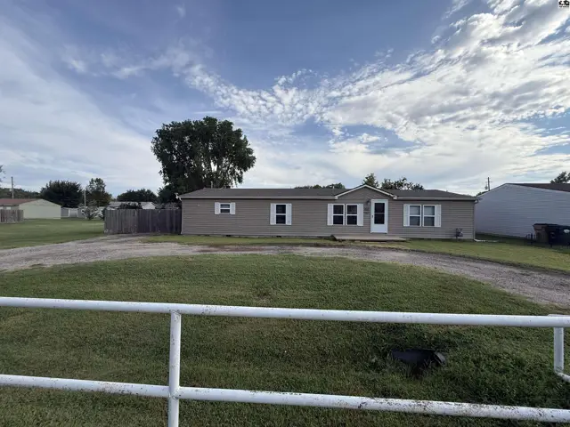 This single-story home features tan siding, white trim, and a gravel driveway.