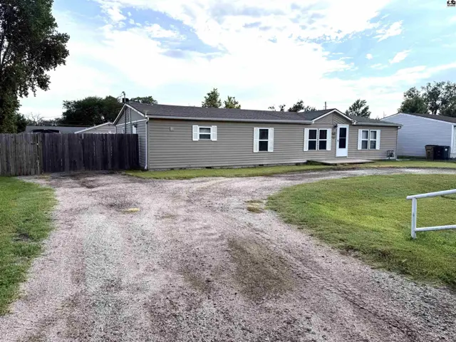 This single-story home features tan siding, white trim, and a gravel driveway.