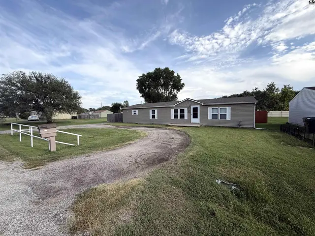 This single-story home features a gravel driveway and a large, grassy yard.