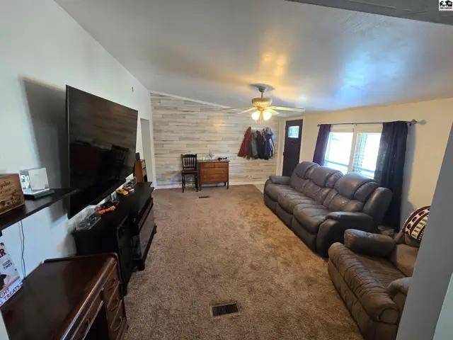 Spacious living room with plush carpeting, a textured accent wall, and a ceiling fan.