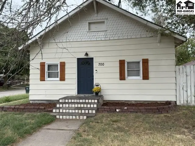 This cream-colored house features a dark blue door, white shutters, and a small front porch.