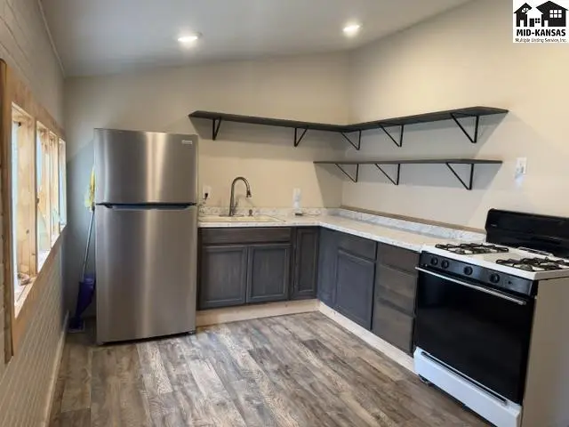 This kitchen features dark wood cabinets, stainless steel appliances, and light wood-look flooring.