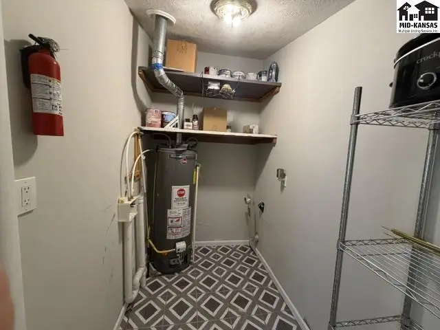 This utility room features a water heater, shelving, and a patterned floor.