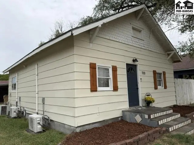 This cream-colored home features wood shutters, a dark blue door, and a small porch.