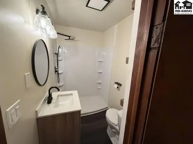 This bathroom features a white tiled shower, vanity with a black faucet, and a toilet.