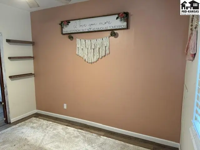 This room features a peach-toned accent wall, two floating shelves, and a patterned rug.