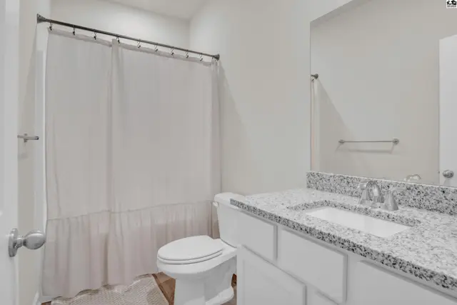 This bathroom features a white toilet, a granite-topped vanity, and a white shower curtain.