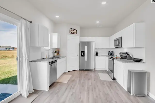 This modern kitchen features white cabinetry, granite countertops, stainless steel appliances, and a sliding glass door.