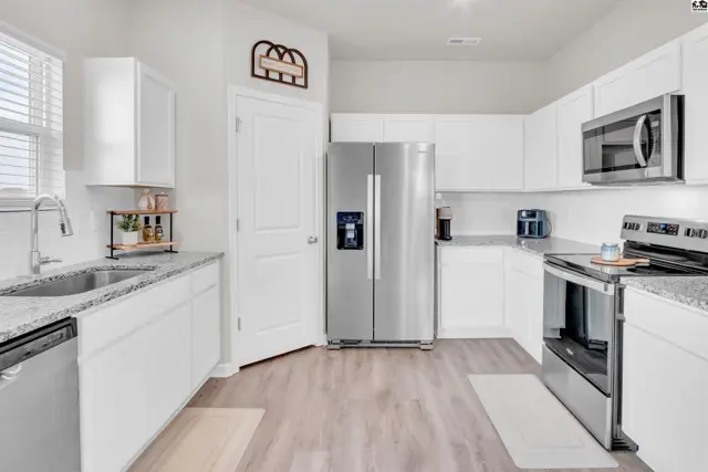 Modern kitchen features white cabinetry, granite countertops, stainless steel appliances, and light wood-look flooring.