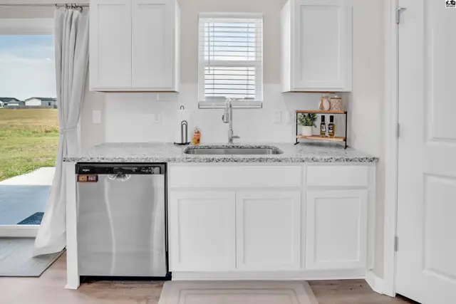 White cabinetry, granite countertops, and a stainless steel dishwasher accent this kitchen.