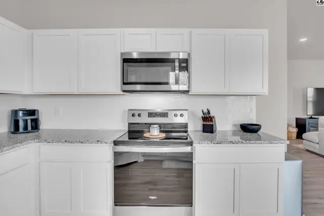 White cabinets and granite countertops surround a stainless steel range and microwave.