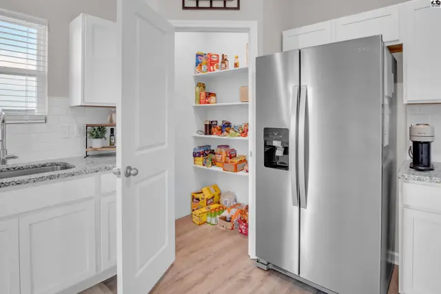 Stainless steel refrigerator stands next to a pantry with shelves stocked with food items.