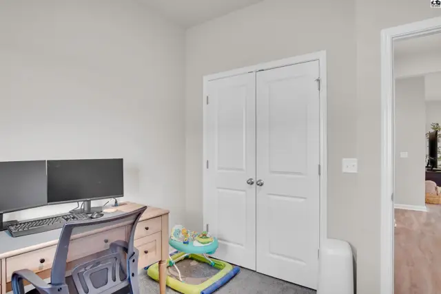 This room features a desk with dual monitors, a closet with double doors, and a doorway to another space.