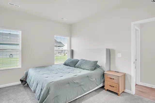This bedroom features a large bed, a nightstand, and two windows with blinds.