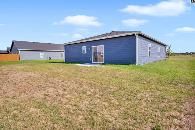 A blue-sided house with a sliding glass door sits on a large, grassy lot.