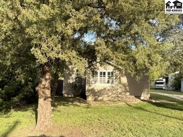 This tan-sided house features a covered porch and mature trees.