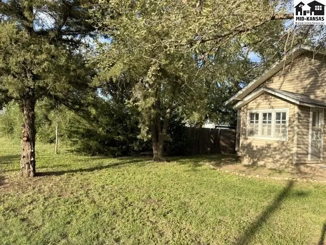 Wood-sided house with a covered porch and large windows sits on a grassy lot.