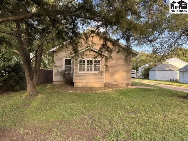 This tan-sided home features a covered front porch and mature trees.