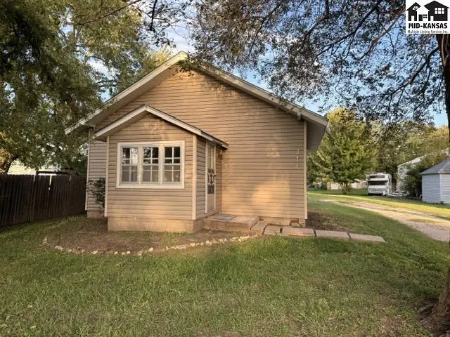 This beige vinyl-sided house features a small covered porch and mature trees.