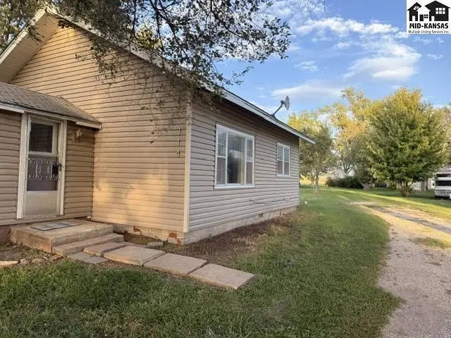 This tan-sided home features a covered front door and a gravel driveway.