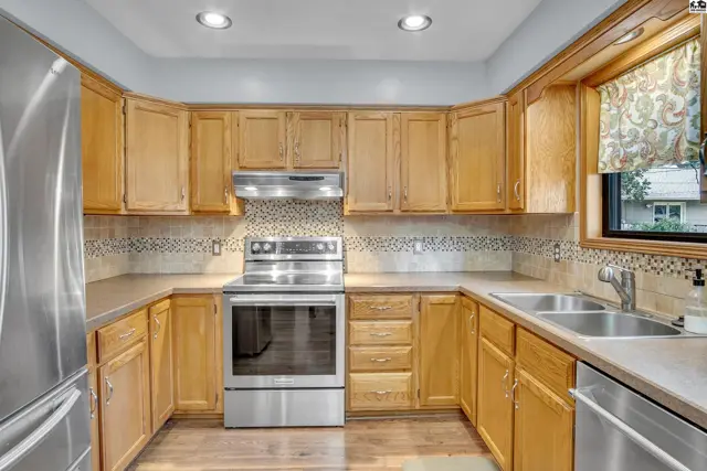 This kitchen features light wood cabinetry, stainless steel appliances, and a tiled backsplash.
