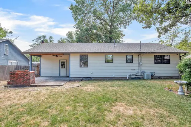 This single-story home features a covered patio, brick outdoor fireplace, and a grassy yard.