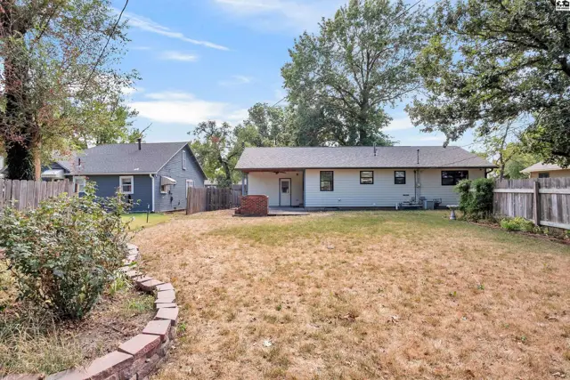 A fenced backyard features a patio, brick fire pit, and mature trees.