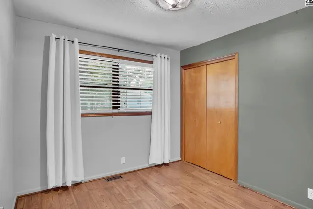 This room features grey walls, a large window with blinds, and a wooden closet.