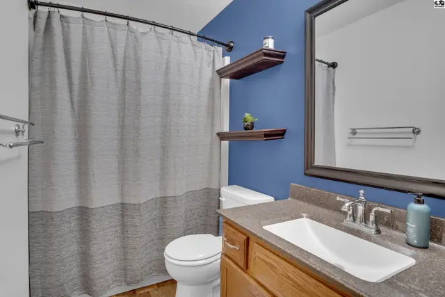 This bathroom features a vanity with a sink, a toilet, and a shower with a grey curtain.