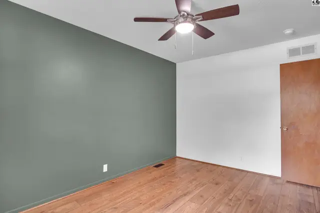 This room features hardwood floors, a ceiling fan, and a painted accent wall.