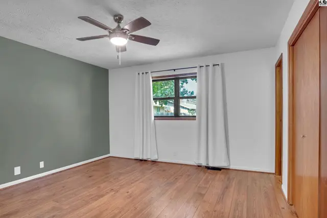 Spacious room with wood-look flooring, a ceiling fan, and a large window.