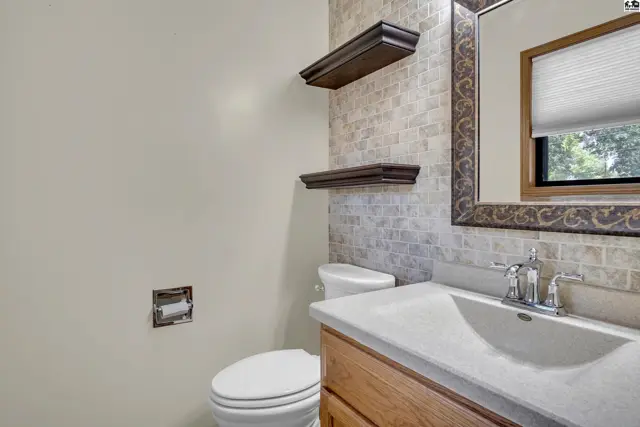 This bathroom features a vanity, toilet, and decorative shelving.