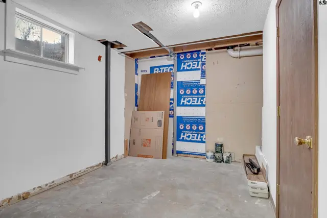 Unfinished basement space with concrete floor, white walls, and exposed ceiling joists.