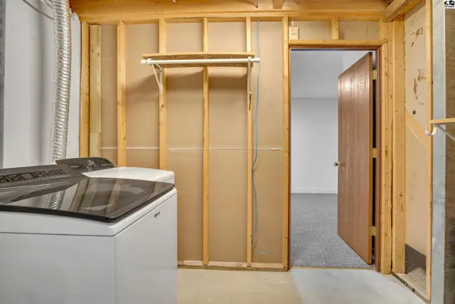 This unfinished basement room features a washing machine, dryer hookups, and a doorway to another room.